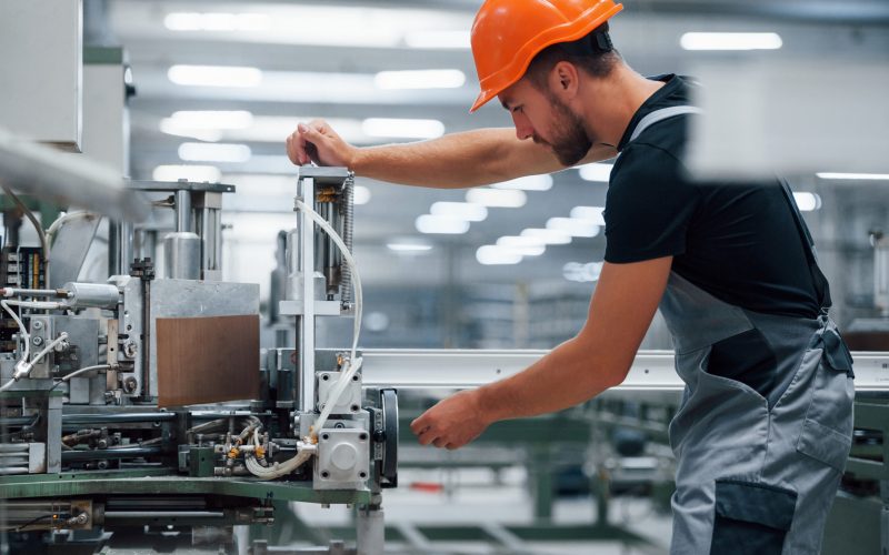Operator of machine. Industrial worker indoors in factory. Young technician with orange hard hat Operator of machine. Industrial worker indoors in factory. Young technician with orange hard hat.